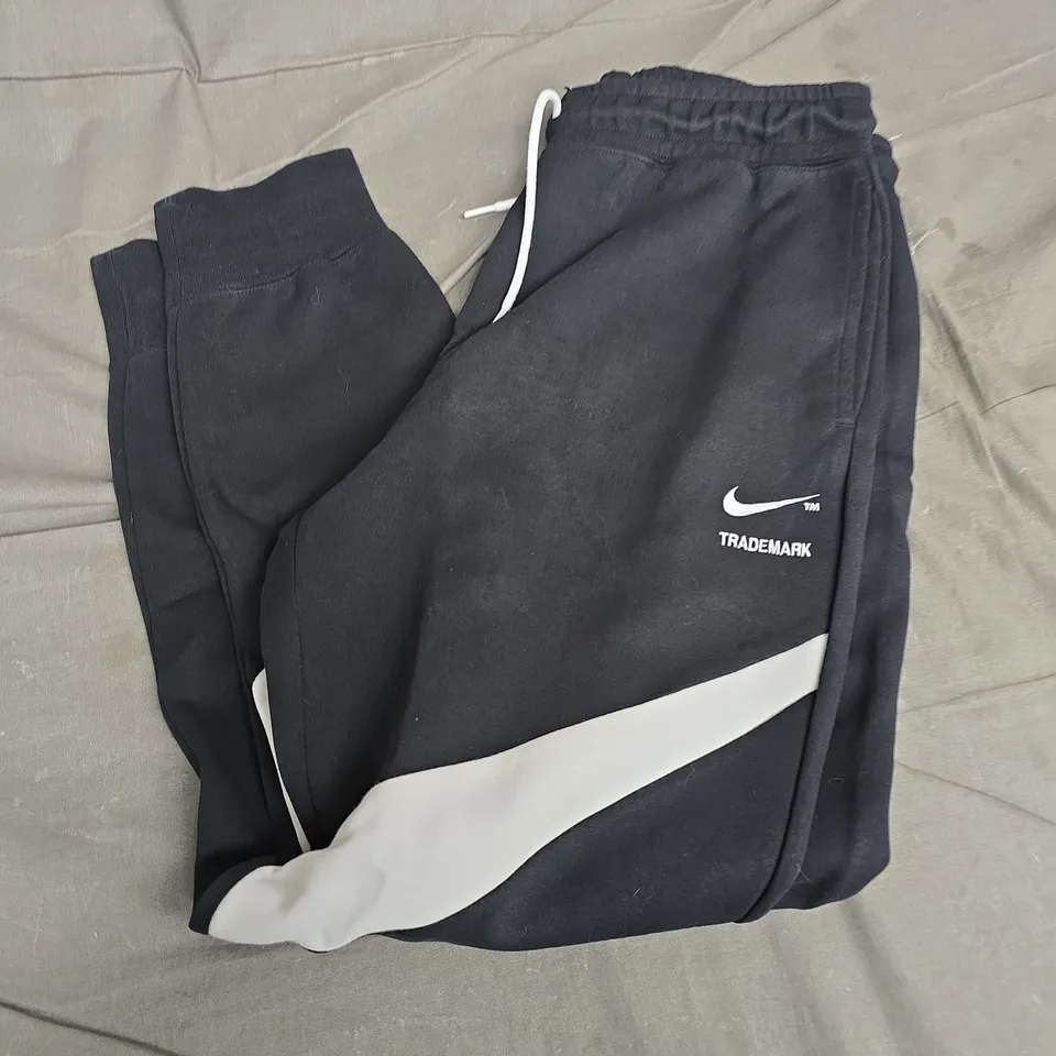 NIKE TRACKPANTS, BLACK WITH WHITE DIAGONAL STRIPE AND SWOOSH – UK MEDIUM (M)