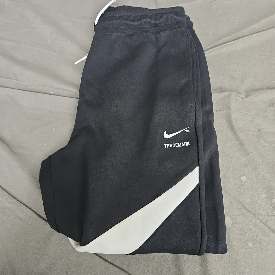NIKE TRACKPANTS, BLACK WITH WHITE DIAGONAL STRIPE AND SWOOSH – UK MEDIUM (M)