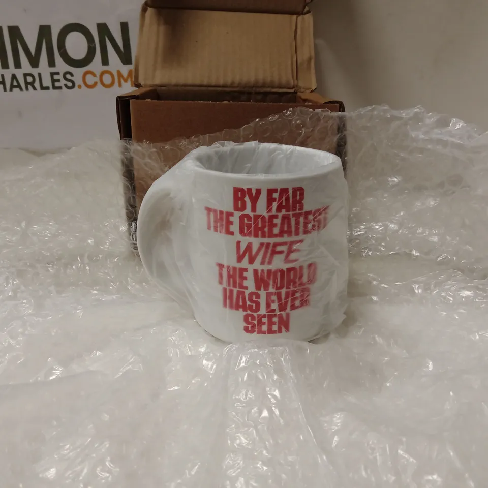 BOXED WHITE CERAMIC MUG WITH RED TEXT READING 'BY FAR THE GREATEST WIFE THE WORLD HAS EVER SEEN'.