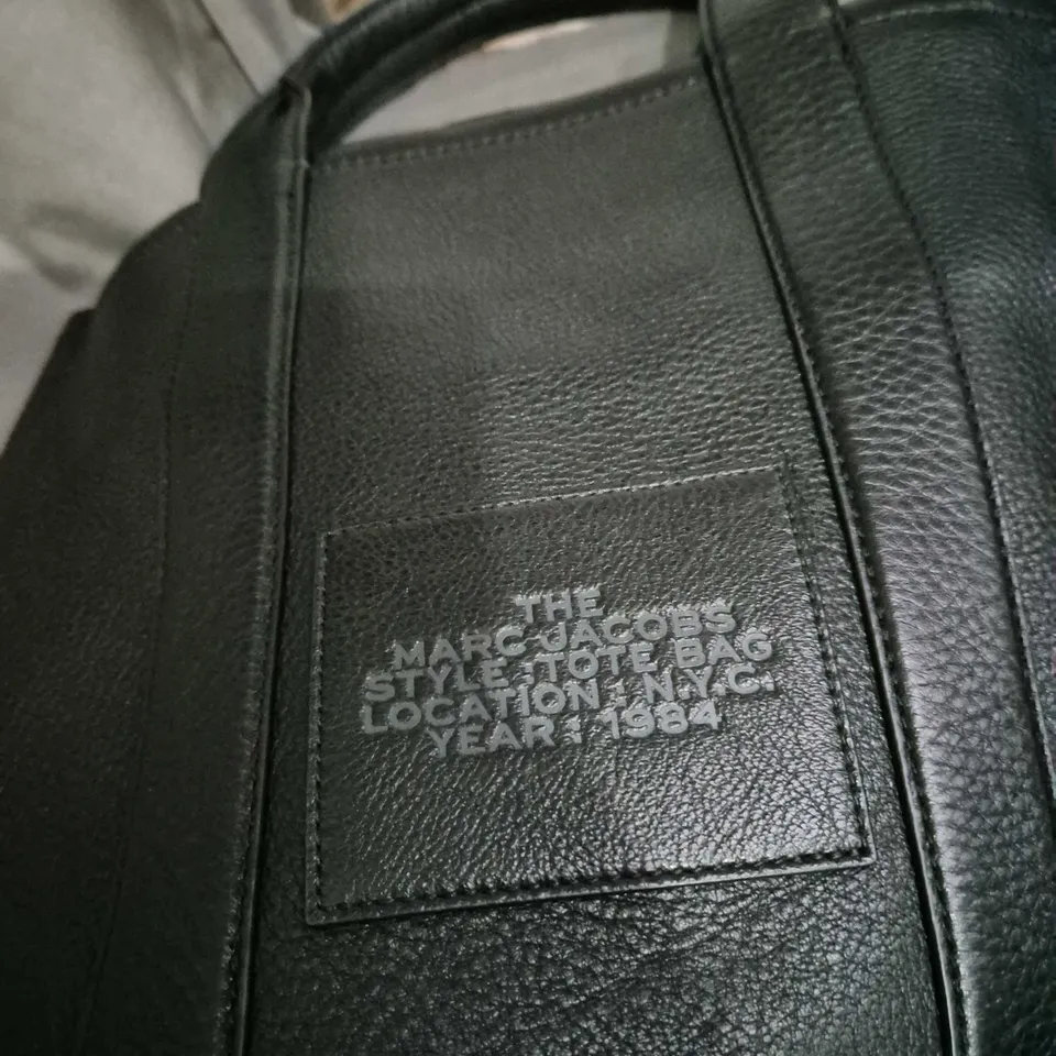 The Marc Jacobs Tote Bag – Black Leather with Front Patch Reading 'THE MARC JACOBS STYLE TOTTE BAG LOCATION NYC YEAR 1984'