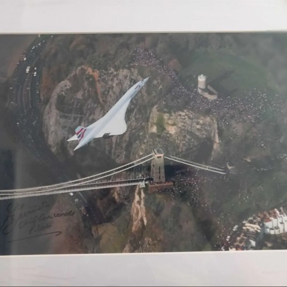 FRAMED AND MOUNTED PHOTOGRAPH OF  THE CONCORDE ON ITS LAST-EVER FLIGHT, OVER THE CLIFTON SUSPENSION BRIDGE IN BRISTOL, WESTERN ENGLAND BY LEWIS WHYLD SIGNED BY CHIEF PILOT CAPTAIN MIKE BANNISTER