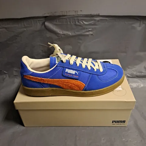 BOXED PAIR OF PUMA SUPER TEAM HANDY TRAINERS IN ULTRA BLUE/RICKIE ORANGE SIZE 7