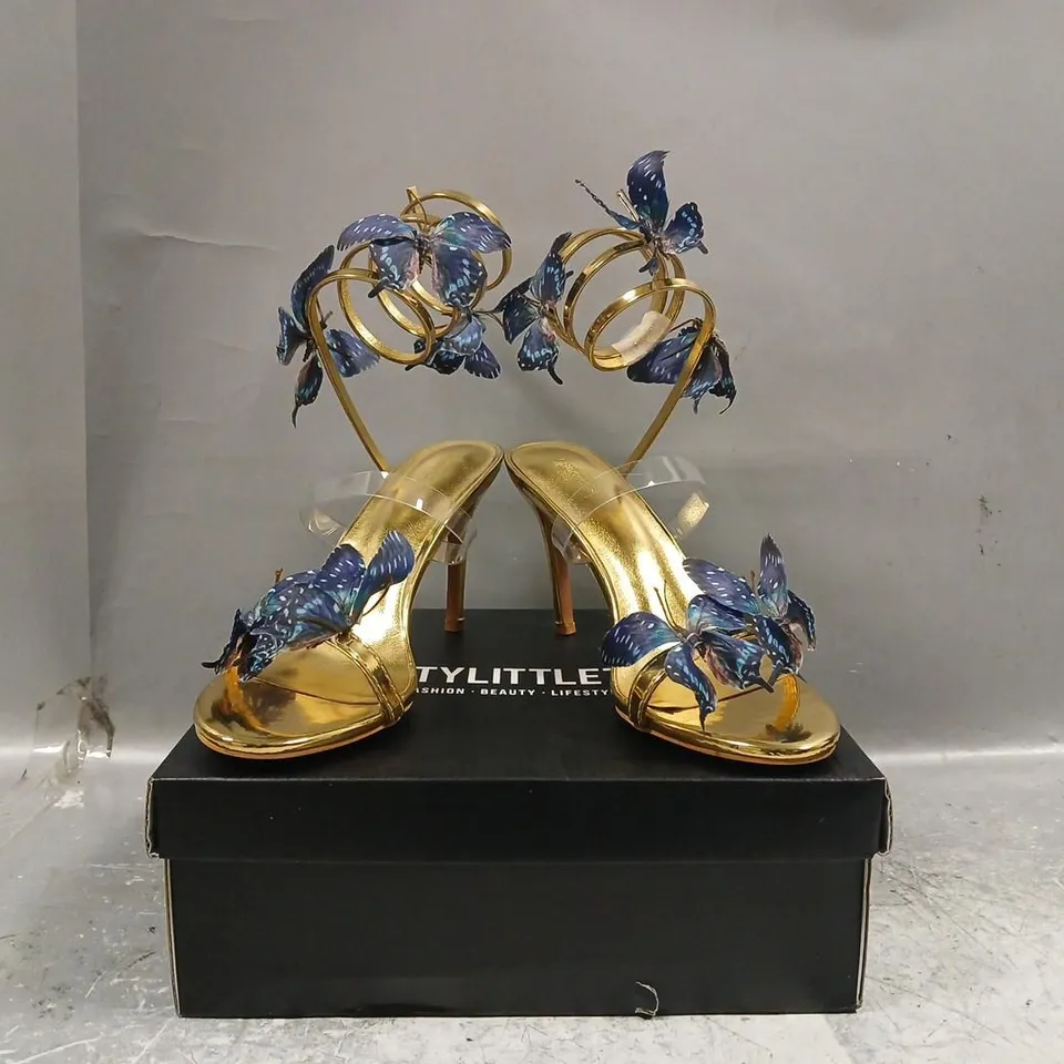 BOXED PAIR OF PRETTY LITTLE THING ROUND TOE BLUE BUTTERFLY SPIRAL STRAP HIGH HEELED SANDALS IN METALLIC GOLD SIZE UK 7