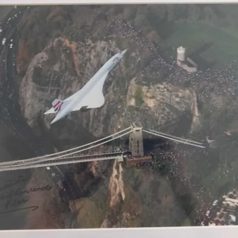 FRAMED AND MOUNTED PHOTOGRAPH OF THE CONCORDE ON ITS LAST-EVER FLIGHT, OVER THE CLIFTON SUSPENSION BRIDGE IN BRISTOL, WESTERN ENGLAND BY LEWIS WHYLD SIGNED BY CHIEF PILOT CAPTAIN MIKE BANNISTER
