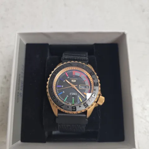 SEIKO 5 AUTOMATIC WRISTWATCH, BLACK DIAL WITH RAINBOW MARKERS, DAY-DATE, GOLD-TONE CASE, NYLON STRAP – IN BOX
