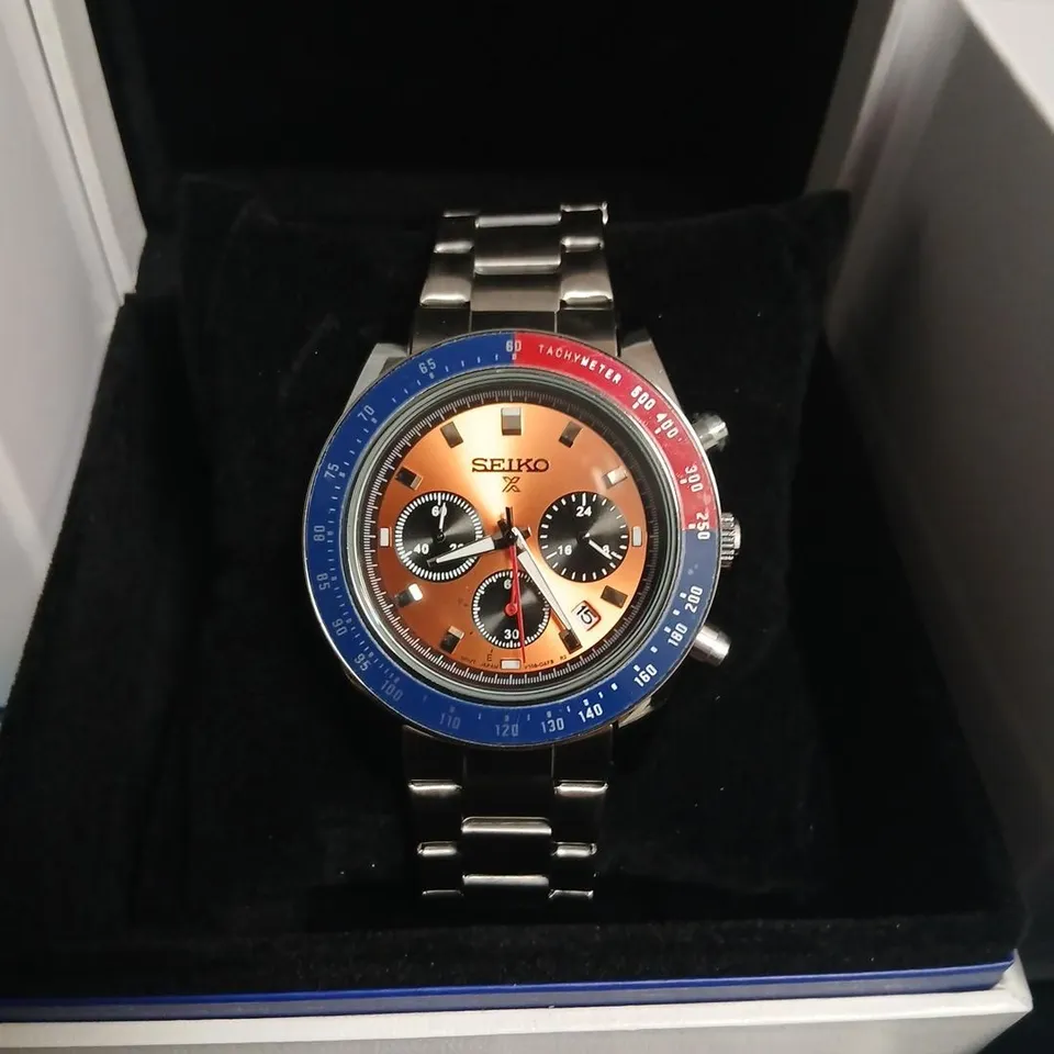 SEIKO CHRONOGRAPH WATCH, STAINLESS STEEL BRACELET, ORANGE DIAL WITH BLUE TACHYMETER BEZEL – BOXED