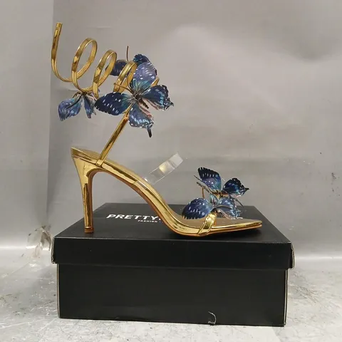BOXED PAIR OF PRETTY LITTLE THING ROUND TOE BLUE BUTTERFLY SPIRAL STRAP HIGH HEELED SANDALS IN METALLIC GOLD SIZE UK 7