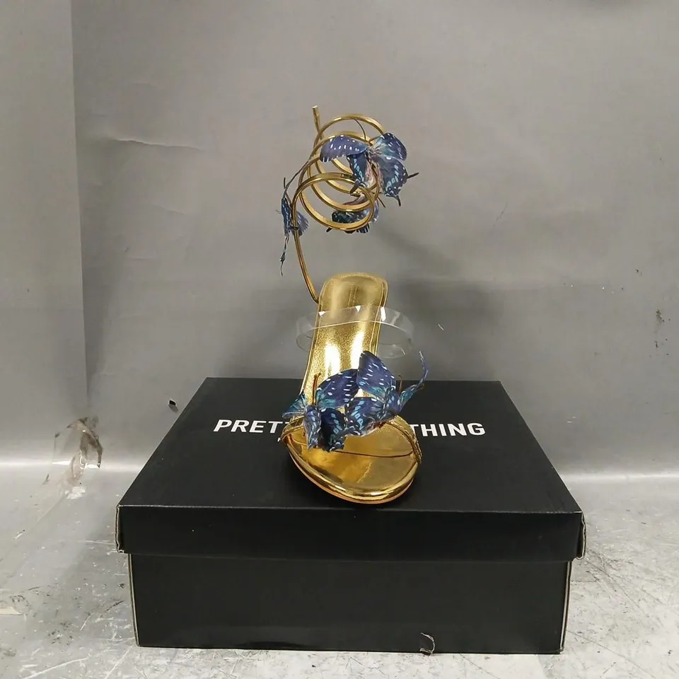 BOXED PAIR OF PRETTY LITTLE THING ROUND TOE BLUE BUTTERFLY SPIRAL STRAP HIGH HEELED SANDALS IN METALLIC GOLD SIZE UK 7