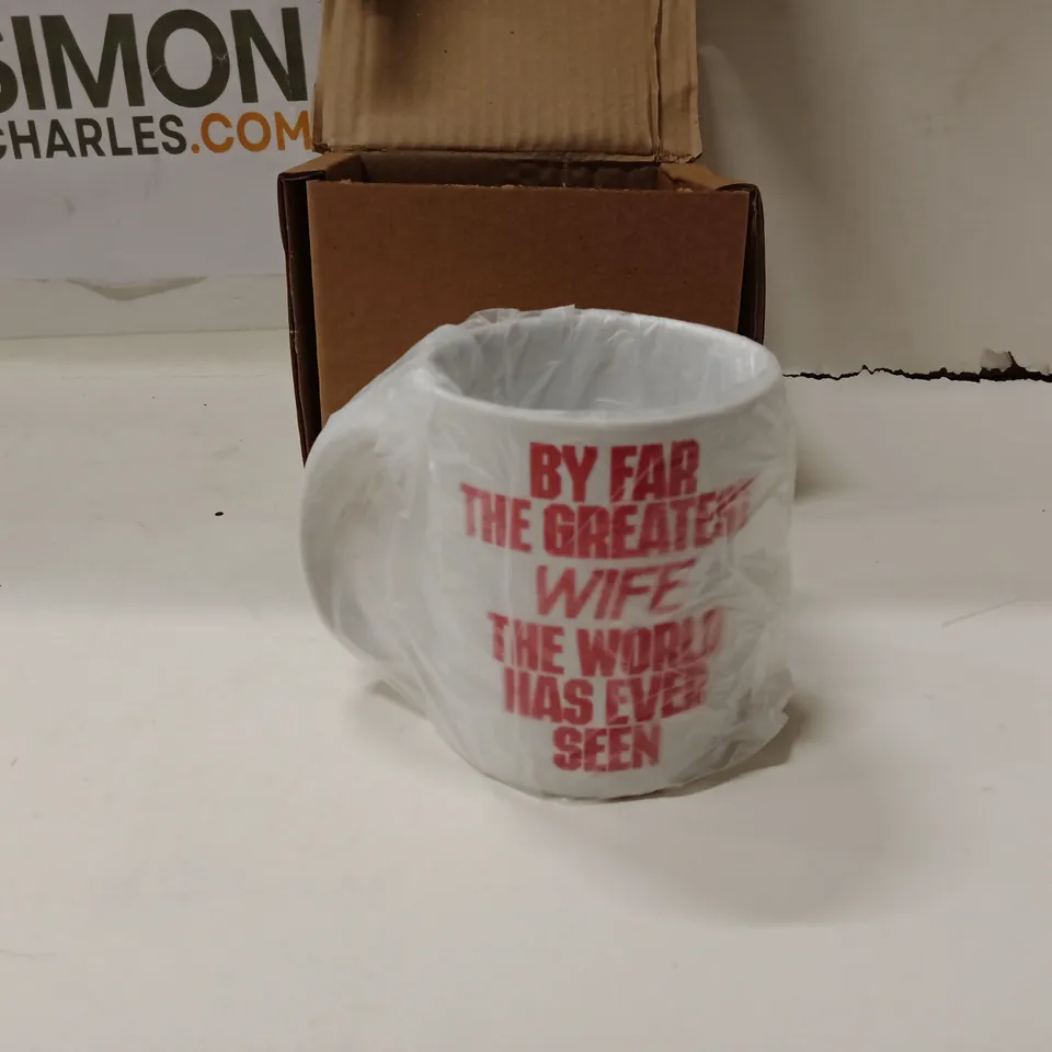 BOXED WHITE CERAMIC MUG WITH RED TEXT READING 'BY FAR THE GREATEST WIFE THE WORLD HAS EVER SEEN'.